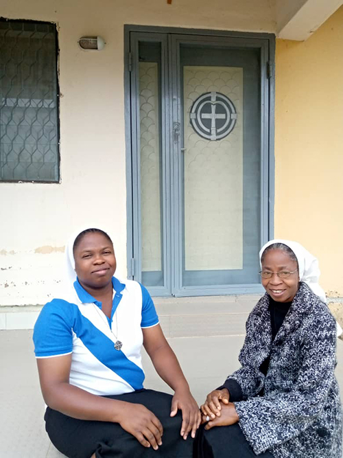 Sister Uzo with a guest seated on front step.